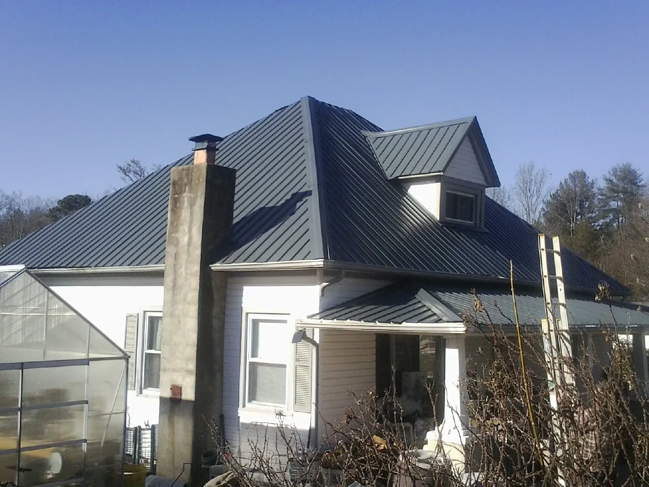 Dark blue standing seam metal roof on a white farmhouse with dormer — Slate & Tile Roof Repair by Roofing Brothers in Elkmont