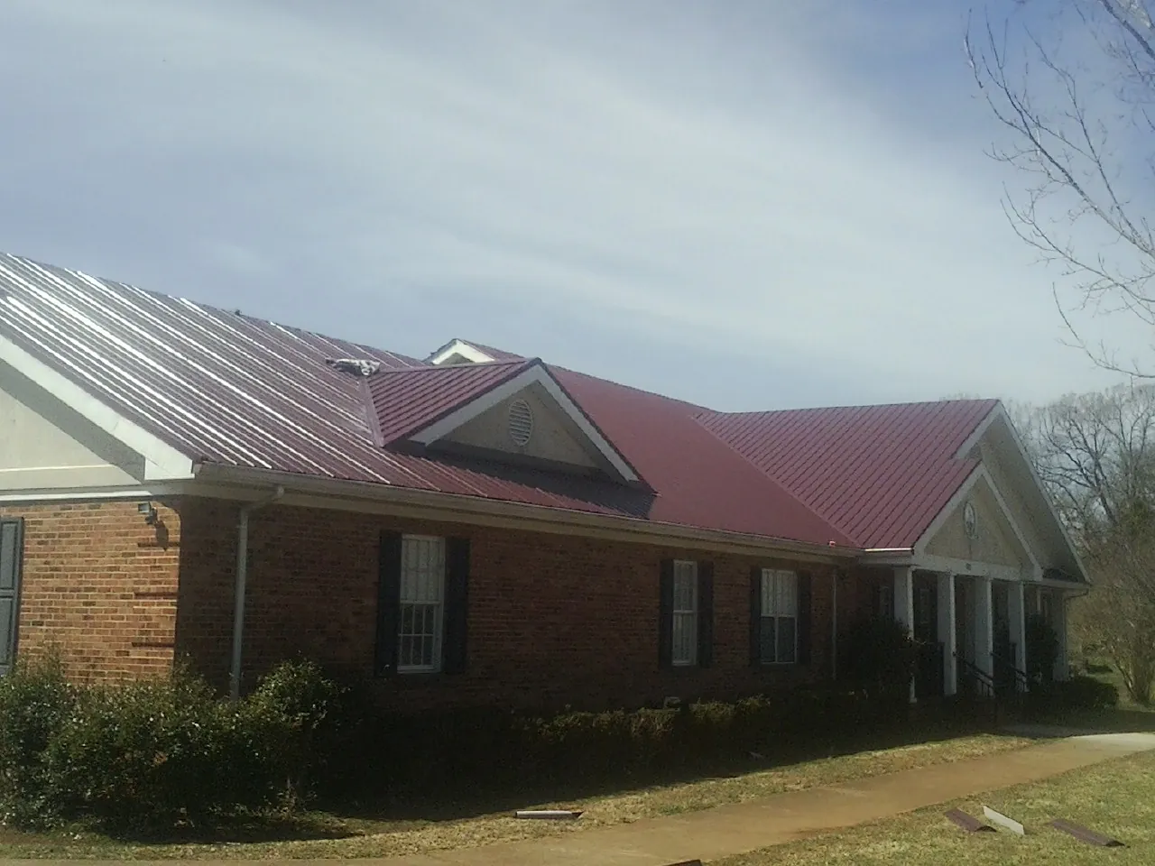 Red metal roof with gabled entries on a long brick building, from a Hail Damage Roof Repair job in Elkmont