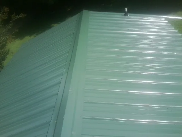 New green metal panels meeting at the ridge of a roof — Flat Roof Repair work by our crew in Elkmont