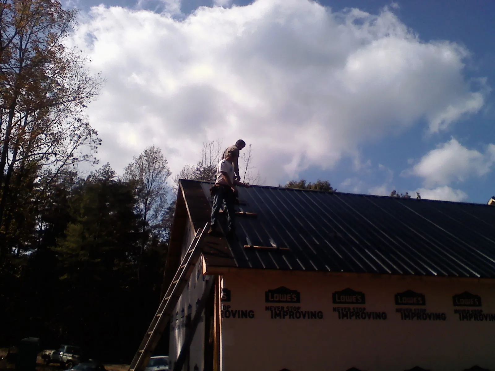 Roofer fastening dark metal panels high against a cloudy sky, from a Roof Inspection job in Elkmont
