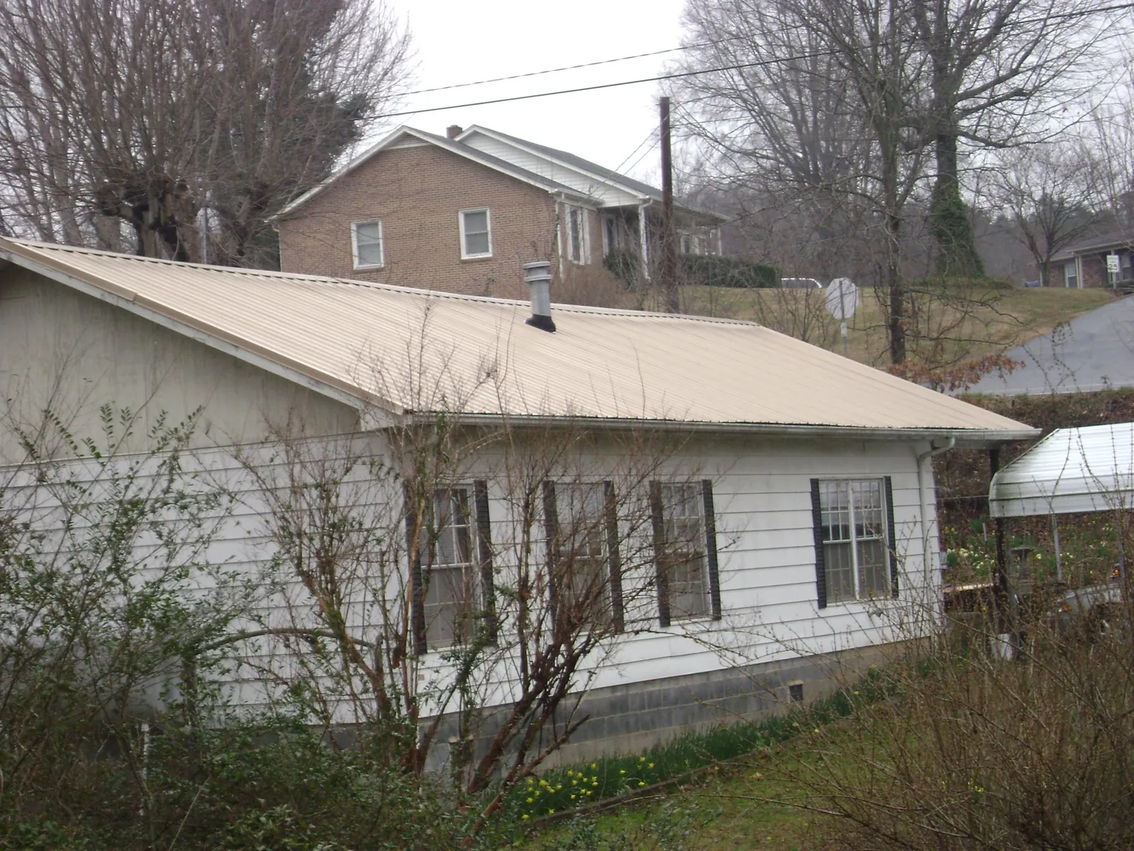 Tan metal roof on a white sided house set into a hillside — Commercial Roofing by Roofing Brothers in Elkmont