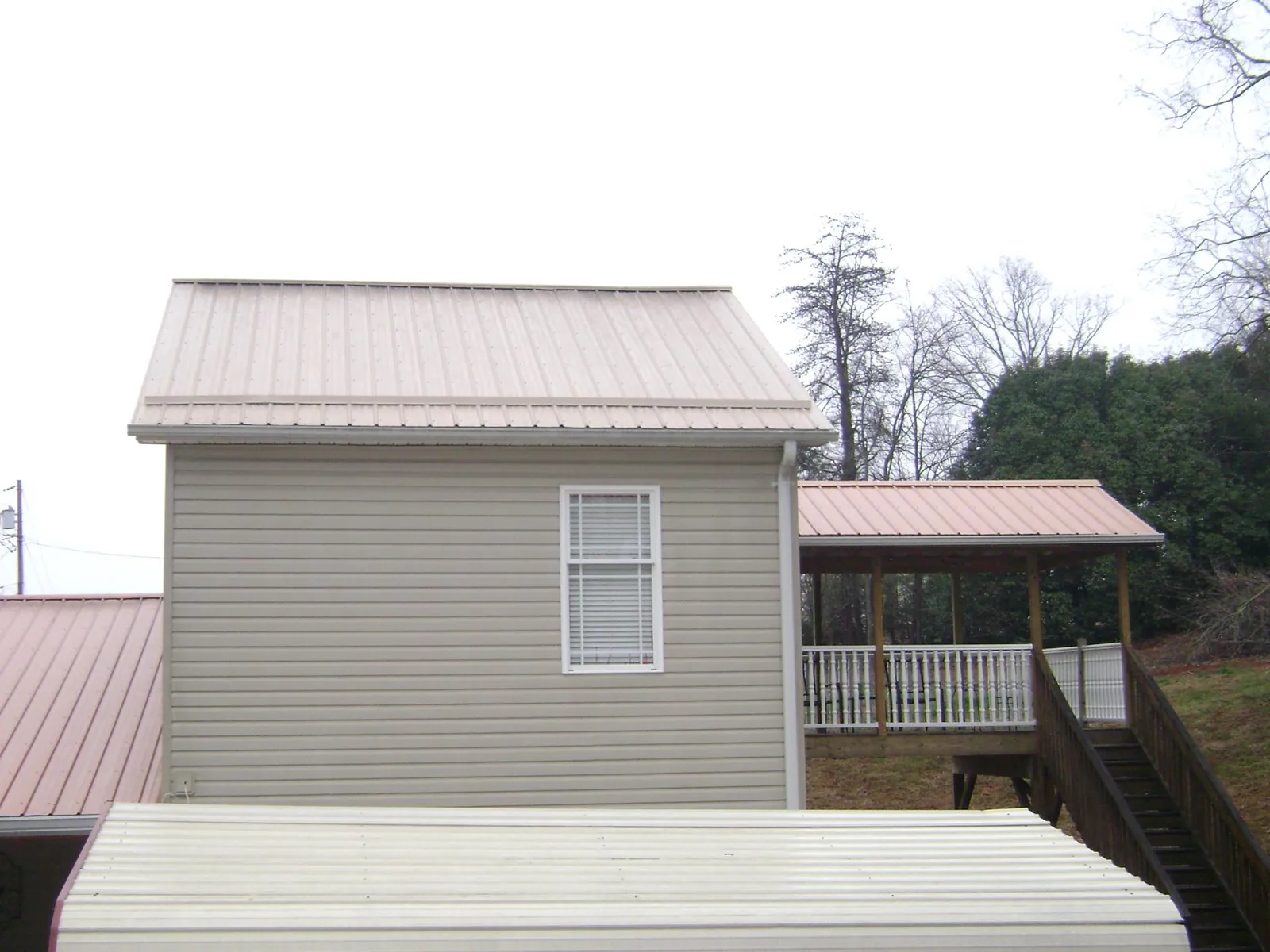 Tan metal roofs on a two story addition and attached porch, from a Roof Replacement job in Elkmont